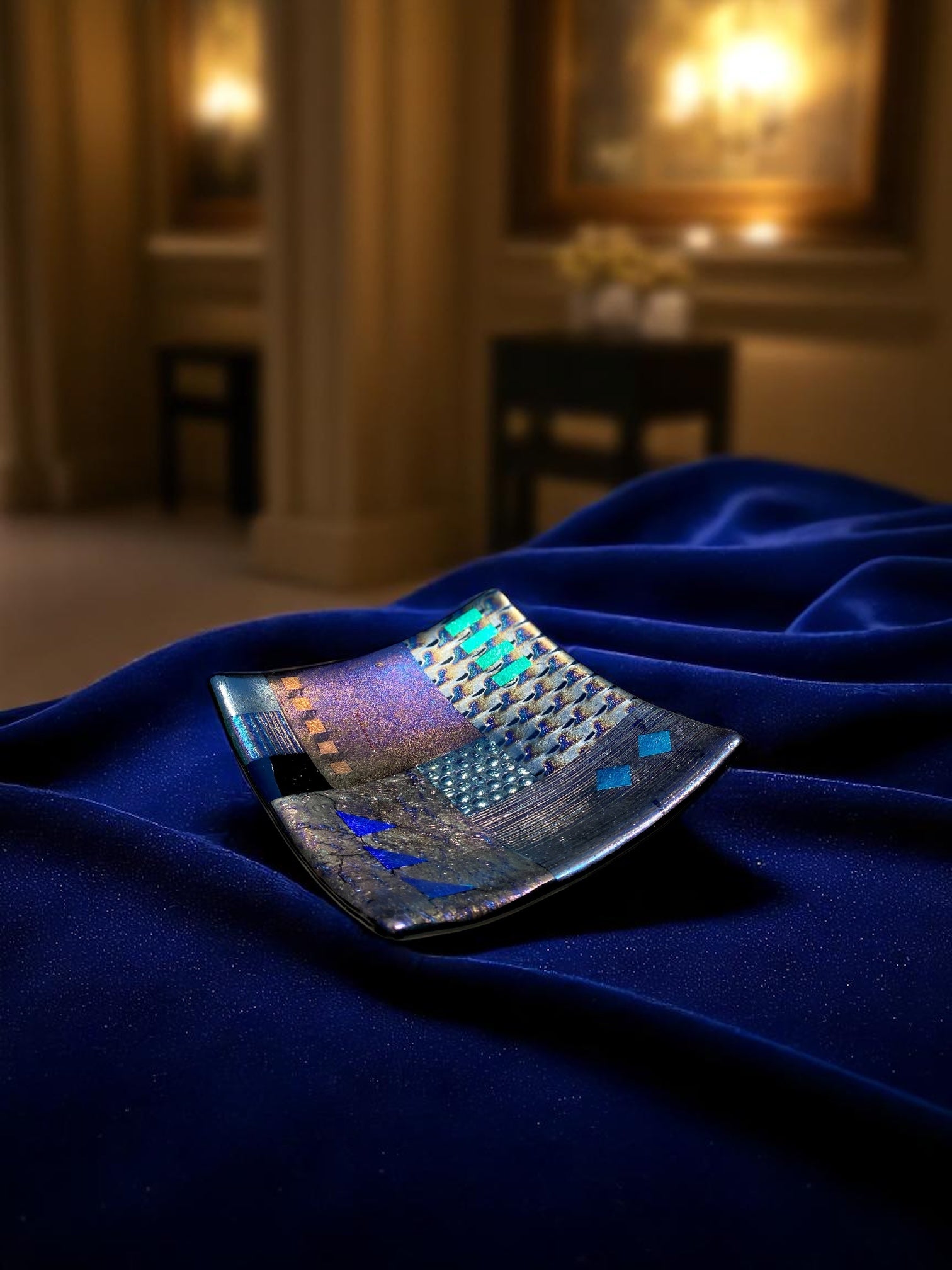 Fused glass piece on a blue fabric with a blurred indoor setting